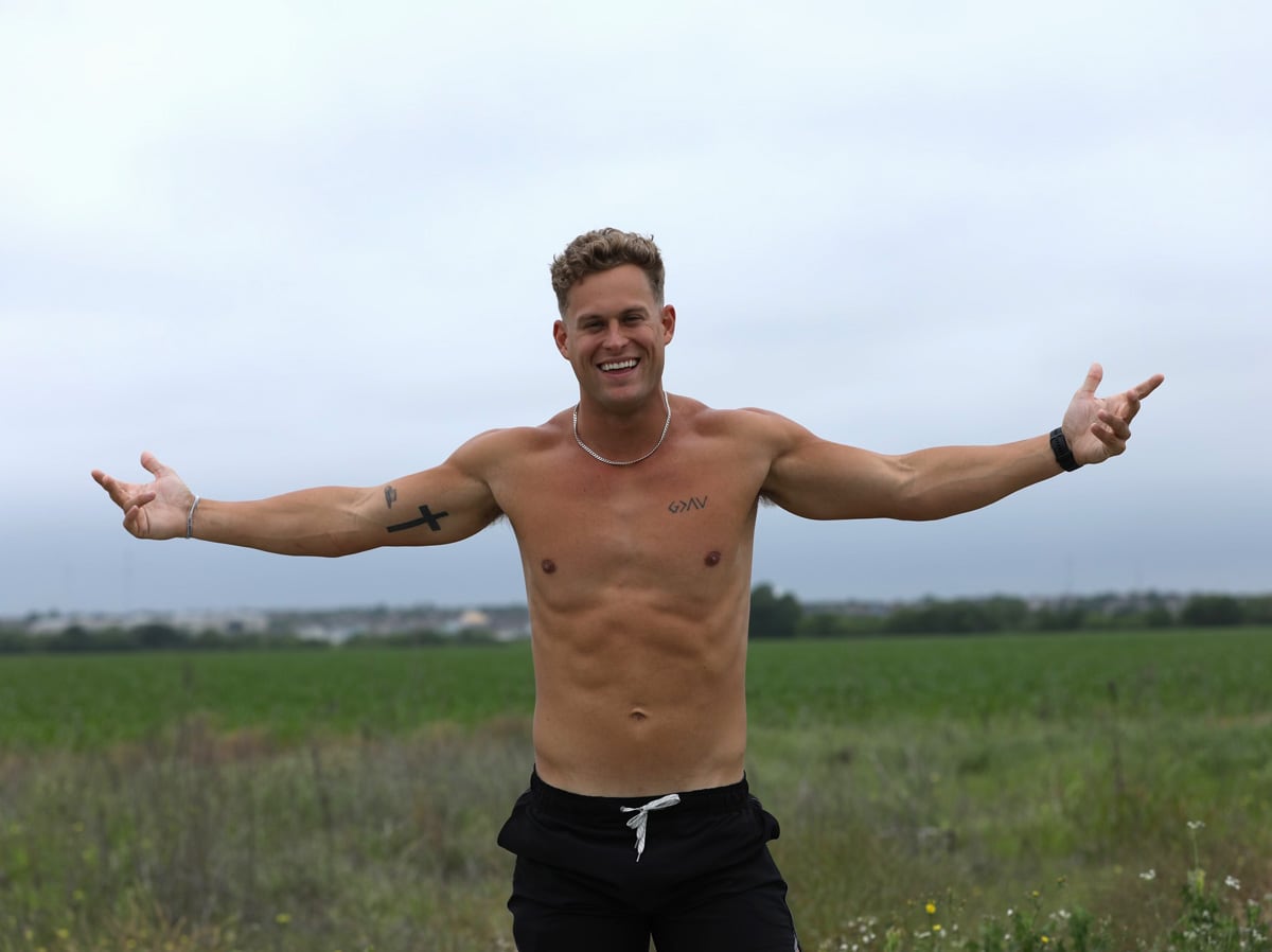 Coach is posing topless with opened arms in the nature.